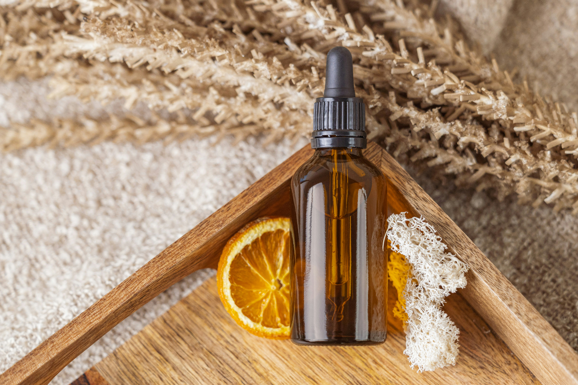Amber glass dropper bottle of essential oil with dried orange slice on a wooden tray