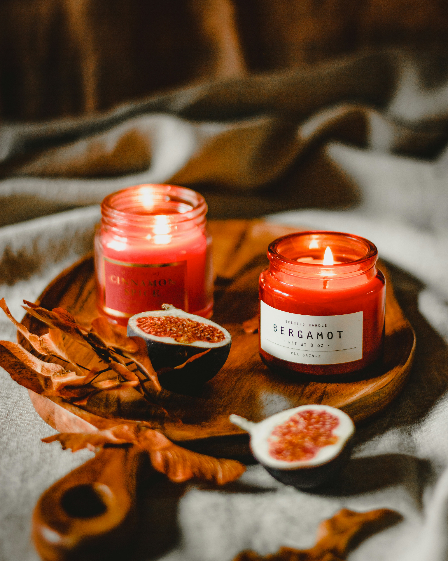 Cinnamon spice and bergamot scented candles on a wooden tray with figs and autumn leaves